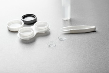 Pair of contact lenses, container, tweezers and bottle with solution on grey background, close up view