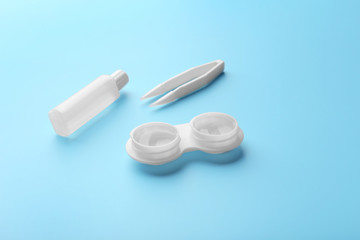 Container with contact lenses, tweezers and bottle of solution on blue background, close up view