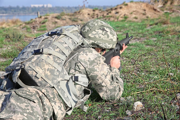 Soldier in camouflage taking aim at military firing range, close up