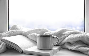 Hot drink with book and plaid on windowsill