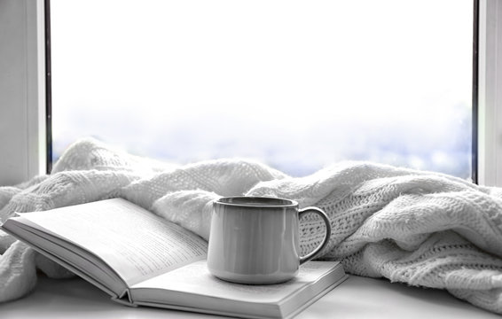 Hot drink with book and plaid on windowsill