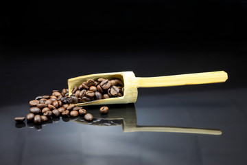 Coffee beans with a wooden scoop on black background.