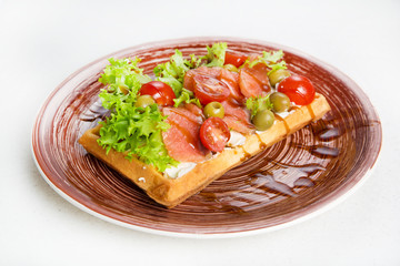 Plate of belgian waffles with salmon, tomatoes, herbs and balsamic vinegar