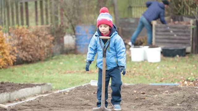 Little boy, shoveling in the garden, digging autumn time