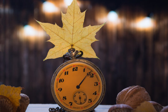 old watch with autumn leaves on the wooden background