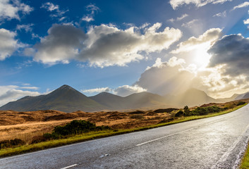Spectacular landscape in Glencoe region, Scotland - spells of sunlight through dramatic clouds, road through the mountains