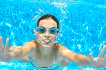 Naklejka premium Child swims in pool underwater, funny happy girl in goggles has fun under water and makes bubbles, kid sport on family vacation 