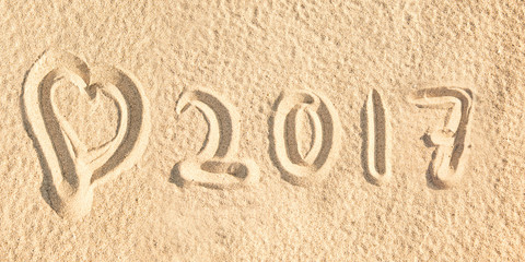 Fototapeta na wymiar Close up on 2017 written in the sand of a beach with a heart