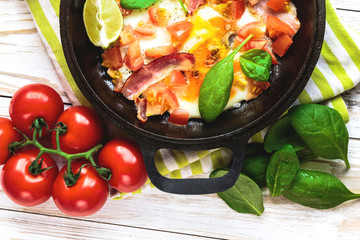 Pan of fried eggs with tomatoes, bacon, spinach, lime