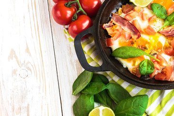 Pan of fried eggs with tomatoes, bacon, spinach, lime