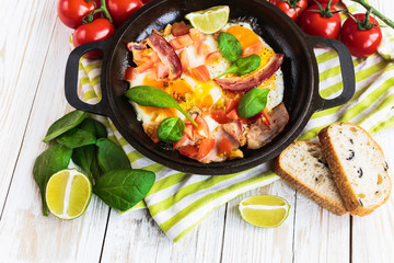 Pan of fried eggs with tomatoes, bacon, spinach, lime