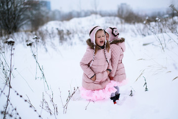 Girls sister in soft pink jacket playing outdoors in winter, sno