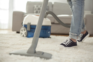 Woman cleaning carpet with a vacuum cleaner in room