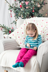 Girl playing with tablet PC near Christmas tree