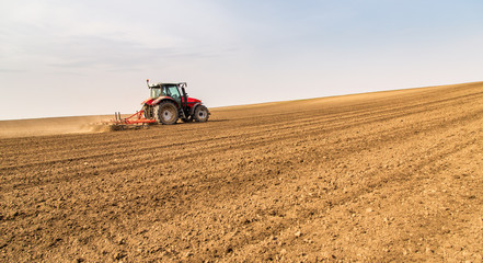 Fototapeta premium Farmer in tractor preparing land with seedbed cultivator