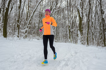 Winter running in forest: happy woman runner jogging in snow, outdoor sport and fitness concept
