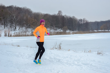 Fototapeta na wymiar Winter running in forest: happy woman runner jogging in snow, outdoor sport and fitness concept 