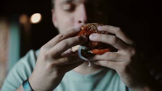 man enjoys eating, tasting the delicious big burger meat with cheese and vegetables