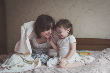 Mom hugs and plays with her daughter hide and seek on  bed, life