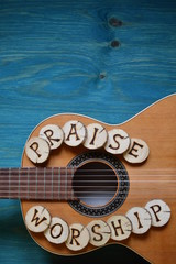guitar on teal wooden background with wood pieces on it lettering the words: PRAISE and WORSHIP