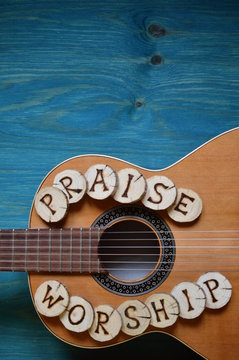 guitar on teal wooden background with wood pieces on it lettering the words: PRAISE and WORSHIP
