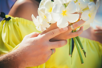man and woman hands hold white bouquet made from tropical flowers