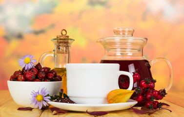 Bowl dog rose , drink , tea, bottle oil on autumn leaves.