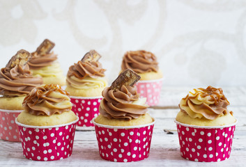 Vanilla cupcakes with a cap of cream on white wooden table