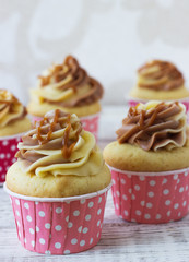Vanilla cupcakes with a cap of cream on white wooden table