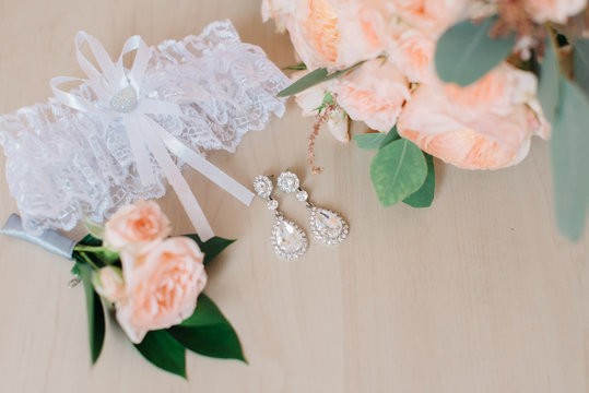 White garter, crystal earrings and prach roses lie on the floor 