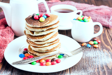 Pancake with colored candy and cup of tea on wooden background