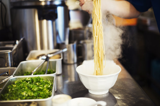 Chef preparing bowls of ramen noodles in broth in kitchen