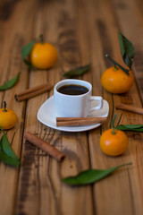 Small white cup of coffee, cinnamon sticks and mandarins on wooden background