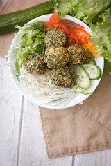Top view of falafel salad in white bowl. Salad include fresh vegetables and falafel