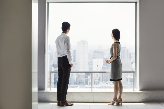 A businessman and businesswoman standing by a large window overlooking a city. 