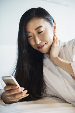 Business woman preparing for work, sitting in bed using her smart phone