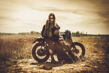 Stylish cafe racer couple on the vintage custom motorcycles in a field