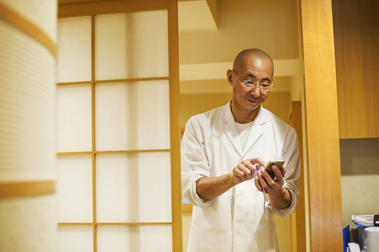 A chef in a small commercial kitchen, an itamae or master chef using a smart phone. 