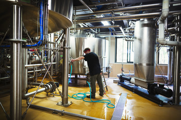 Man working in a brewery adjusting and checking the machinery which transfers the brewed beer around the processing plant. 