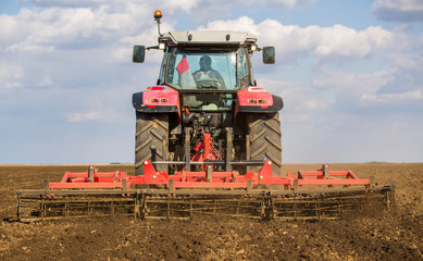 Obraz premium Farmer in tractor preparing land with seedbed cultivator