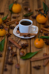 Small white cup of coffee, cinnamon sticks, star anise, hazelnuts and mandarins on wooden background