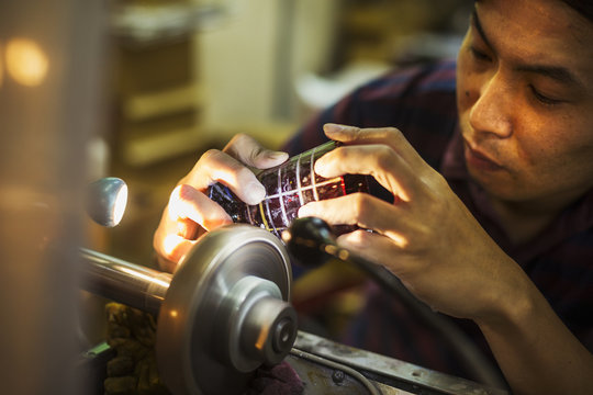 A craftsman at work at a machine, etching or scoring a coloured glass object. 