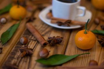 Small white cup of coffee, cinnamon sticks, star anise, hazelnuts and mandarins on wooden background