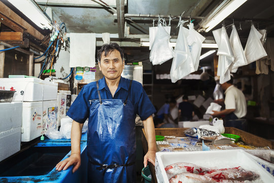 A traditional fresh fish market in Tokyo. A man in a blue apron standing behind the counter of his stall. 