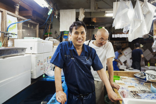 A traditional fresh fish market in Tokyo. Two men in aprons working on a fresh produce stall. 