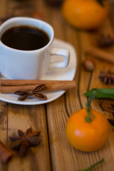Small white cup of coffee, cinnamon sticks, star anise, hazelnuts and mandarins on wooden background