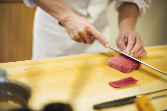 A chef working in a small commercial kitchen, an itamae or master chef slicing fish with a large knife for making sushi