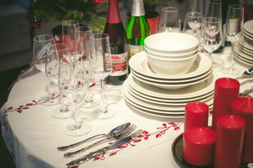 festive table appointments. Christmas table layout, preparation for celebration. Round table covered with tablecloth with an ornament on table arranged plates, dishes, knives, forks, glasses, drinks.