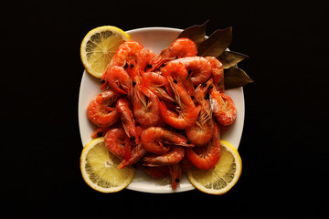 Fresh, delicious, juicy, grilled shrimp with lemon and spices in a white plate on a black table.