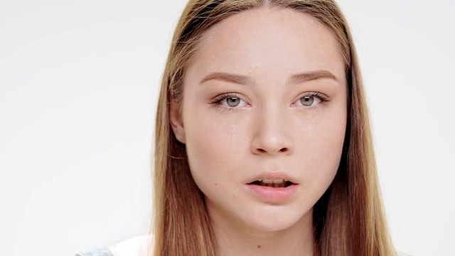 Sad young beautiful girl over crying white background. Slow motion.
